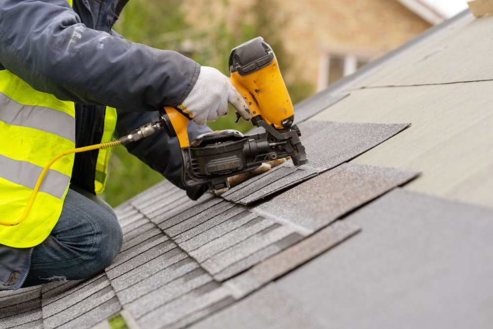 professional roofer fixing residential roof shingle with nail gun